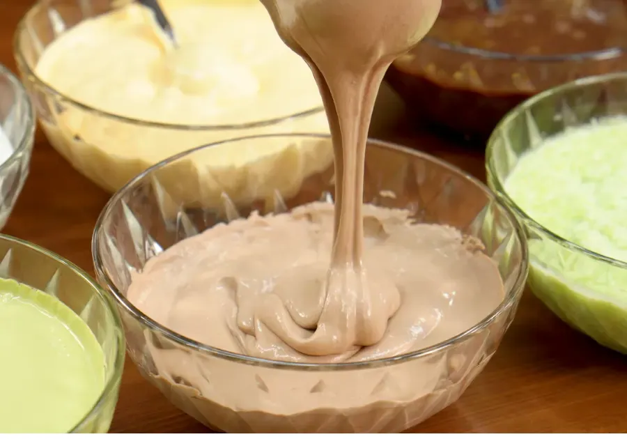Sốt kem dẻo đang được rót vào bát, xung quanh là các bát sốt kem matcha, socola và phô mai